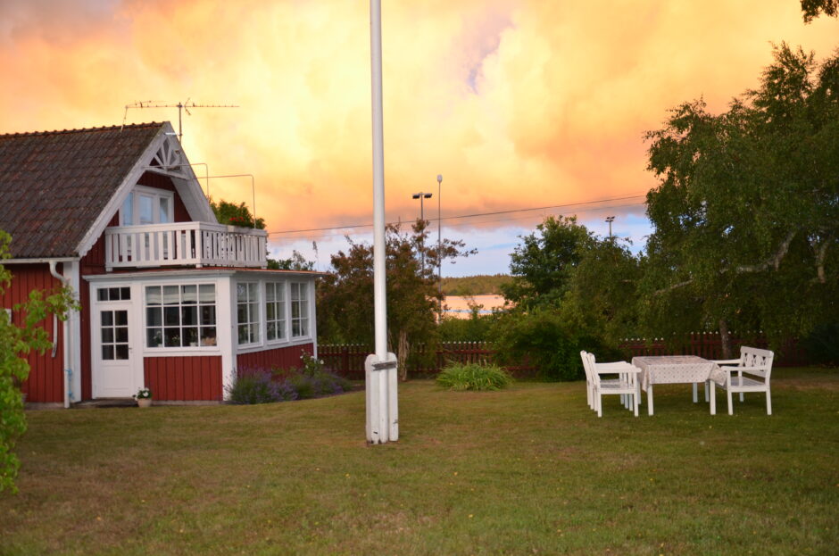 Rött hus med vita knutar, flaggstång och utemöblemang med vacker, färgrik himmel i